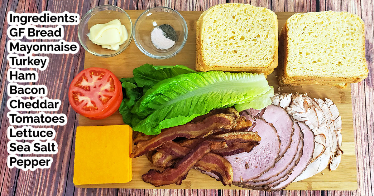 All of the ingredients to make a club sandwich laid out on a wood cutting board.