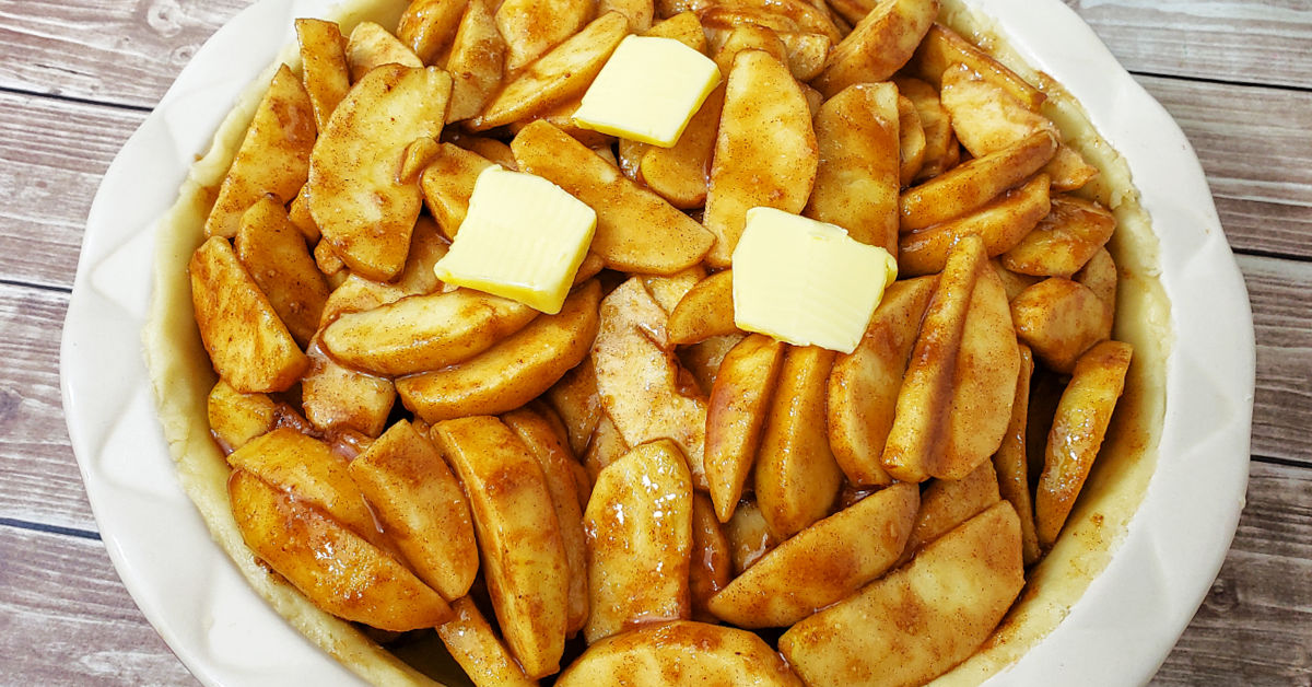 Coated apple slices in pie pan topped with 3 pats of butter.