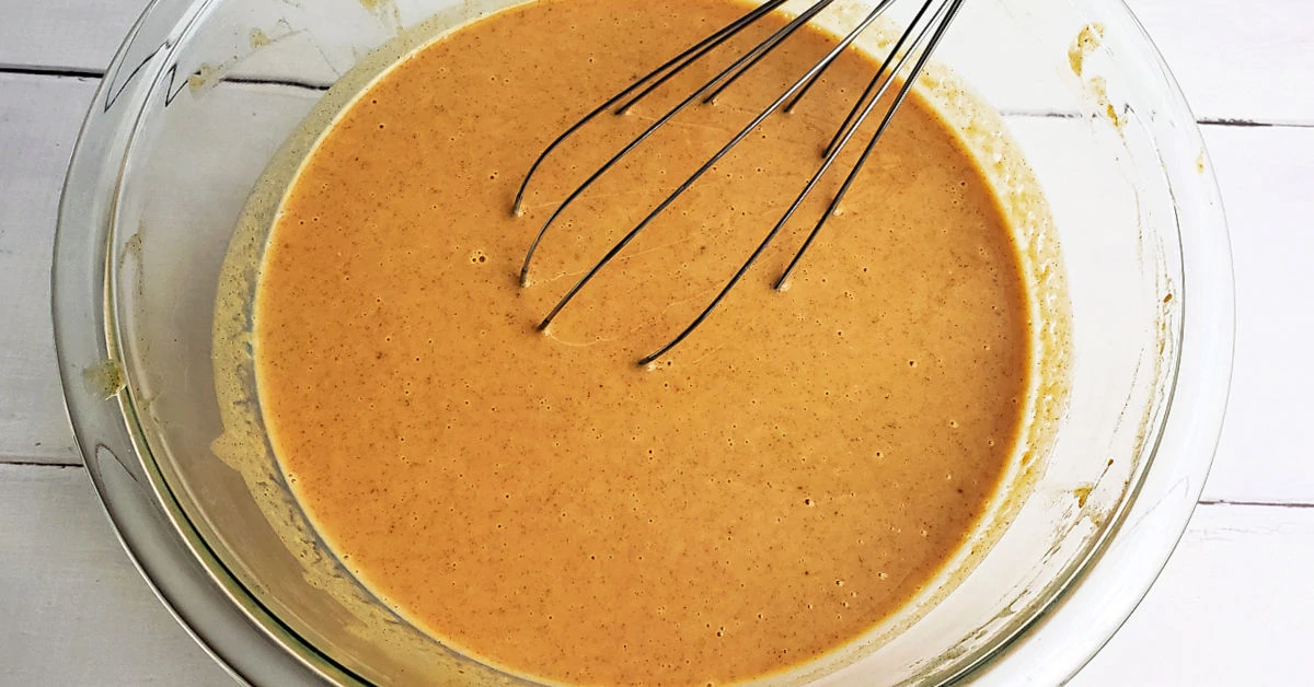 Pumpkin pie filling being whisked together in a glass mixing bowl.