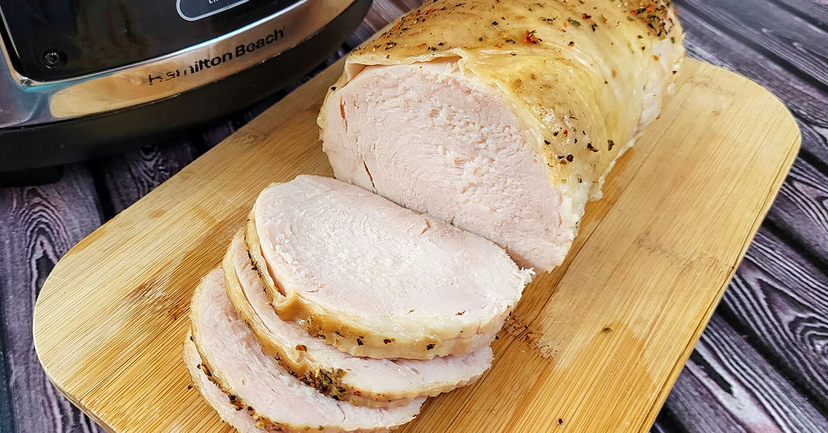 Boneless turkey breast roast resting on cutting board next to a slow cooker.