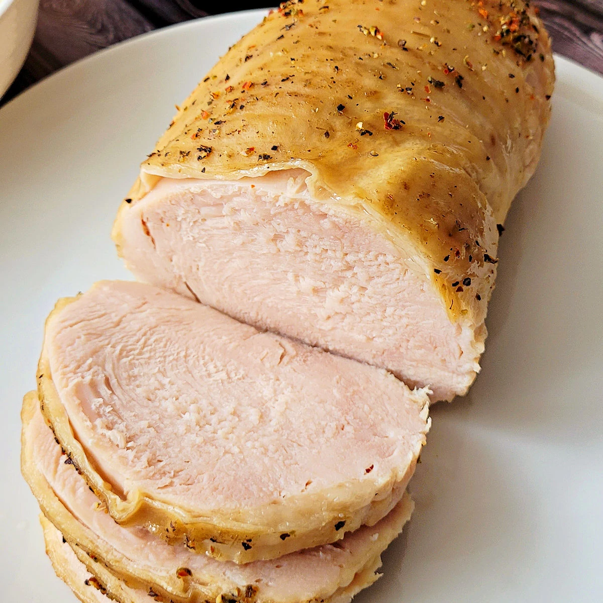 Slow cooker turkey breast sliced and served on a white plate.