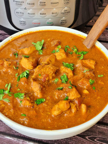 Bowl of homemade butter chicken with a serving spoon on the table in front of an Instant Pot.