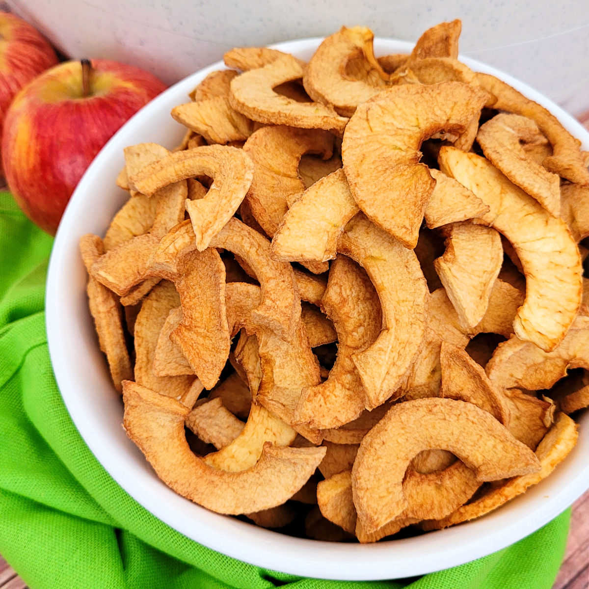 Close up overhead view of dehydrated apple chips in a white serving bowl.