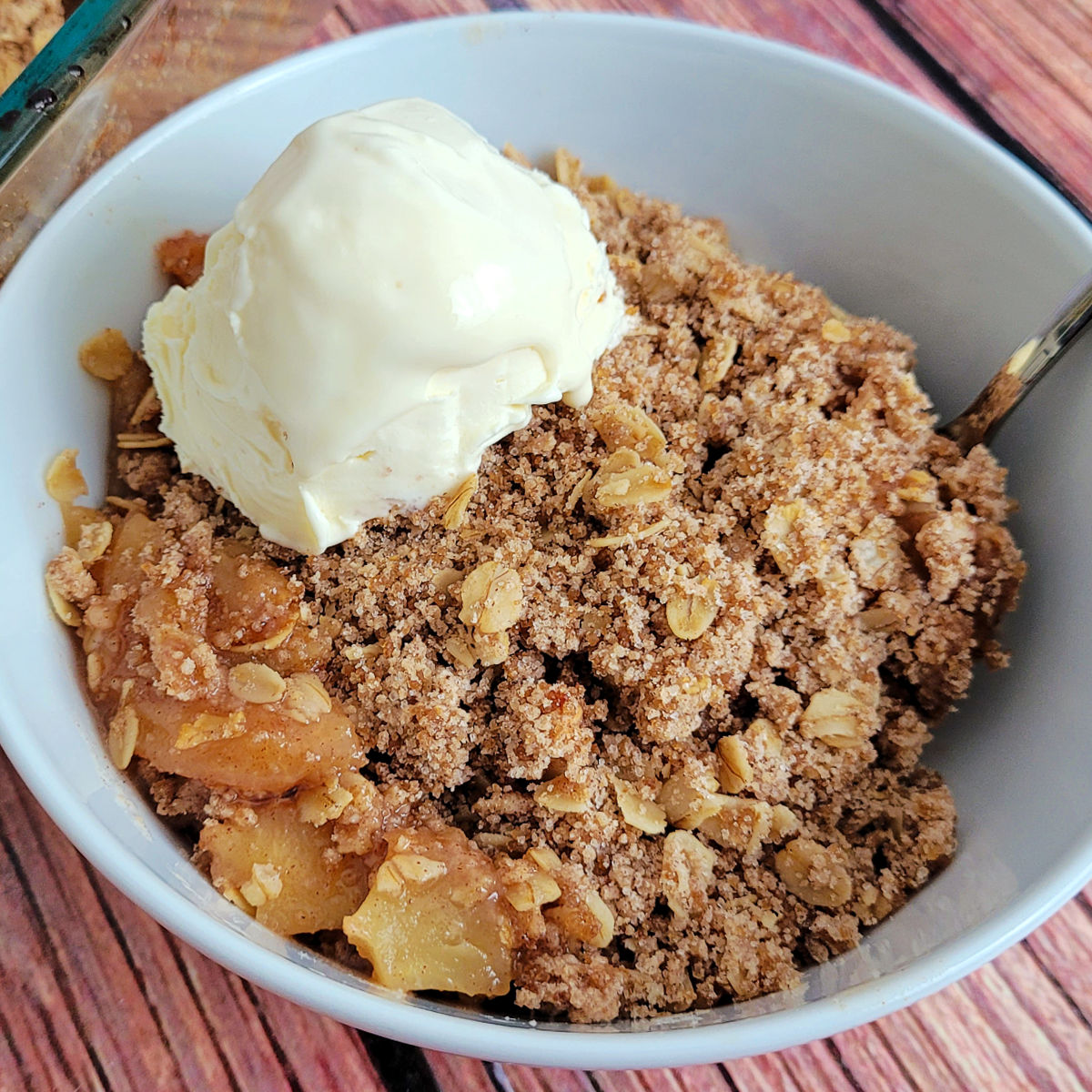 Gluten free apple crisp topped with vanilla ice cream in a small bowl.