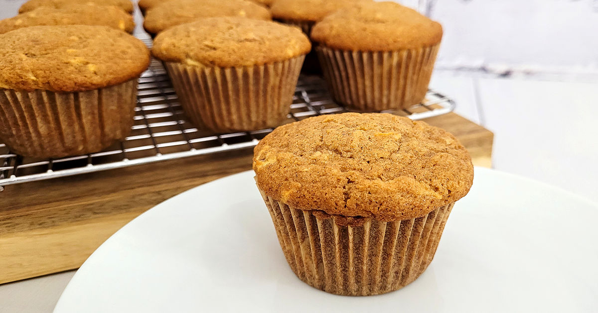 Gluten free apple muffins served on a white dessert plate; set next to the cooling rack of more muffins.