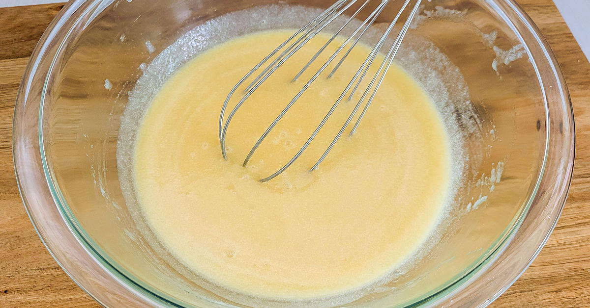 Butter, applesauce, sugar and eggs being whisked together in a large glass mixing bowl.