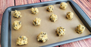 Chocolate chip cookie dough balls laid out on a parchment paper lined baking sheet.
