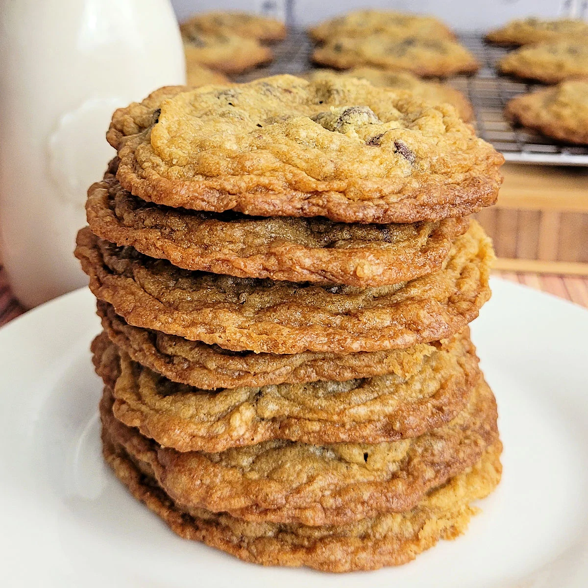 Stack of 7 gluten free chocolate chip cookies on a white dessert plate with a glass of milk.