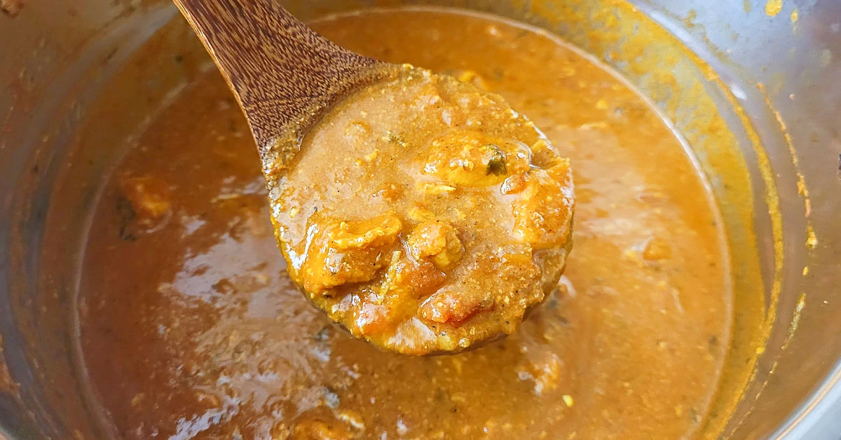 Butter chicken being ladled out of an Instant Pot into a serving bowl.