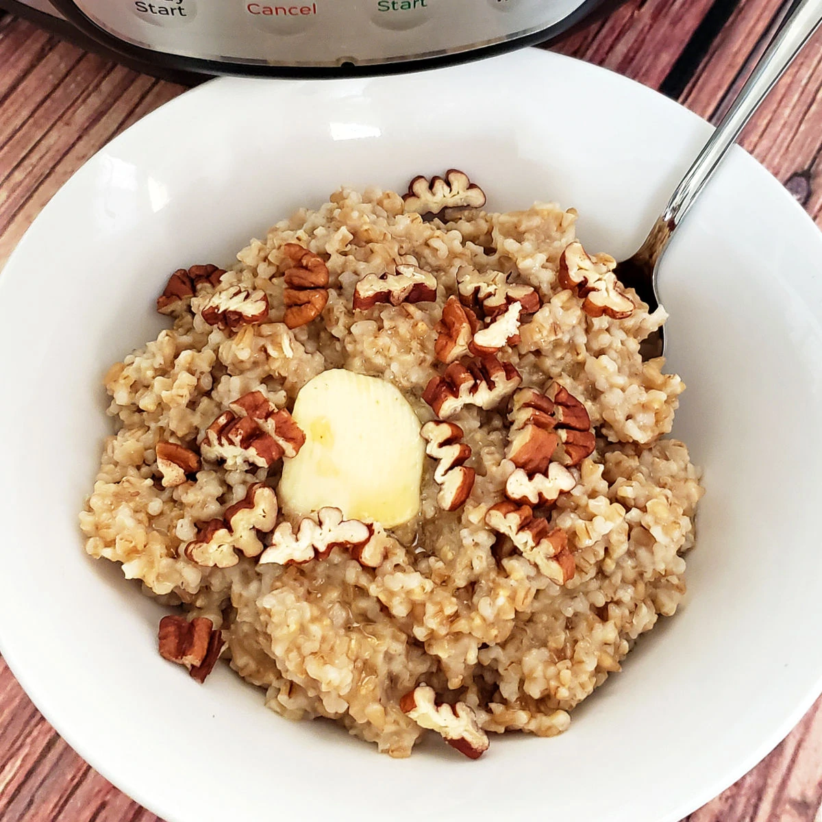 White bowl filled with steel cut oats, topped with pecans, butter and maple syrup.