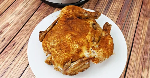 Whole chicken with crispy skin on a white serving plate.