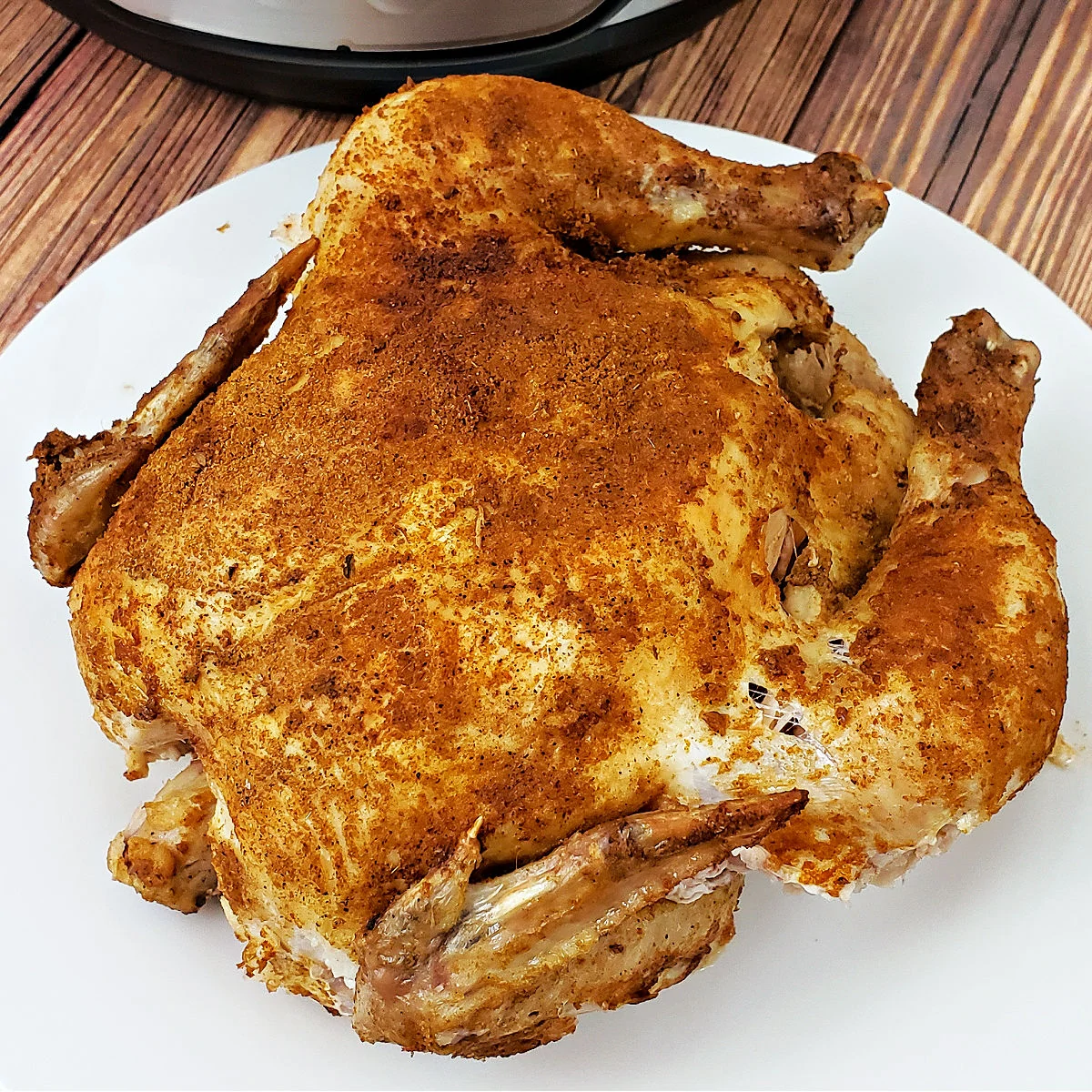 Whole chicken with cajun seasoning on a white serving platter.