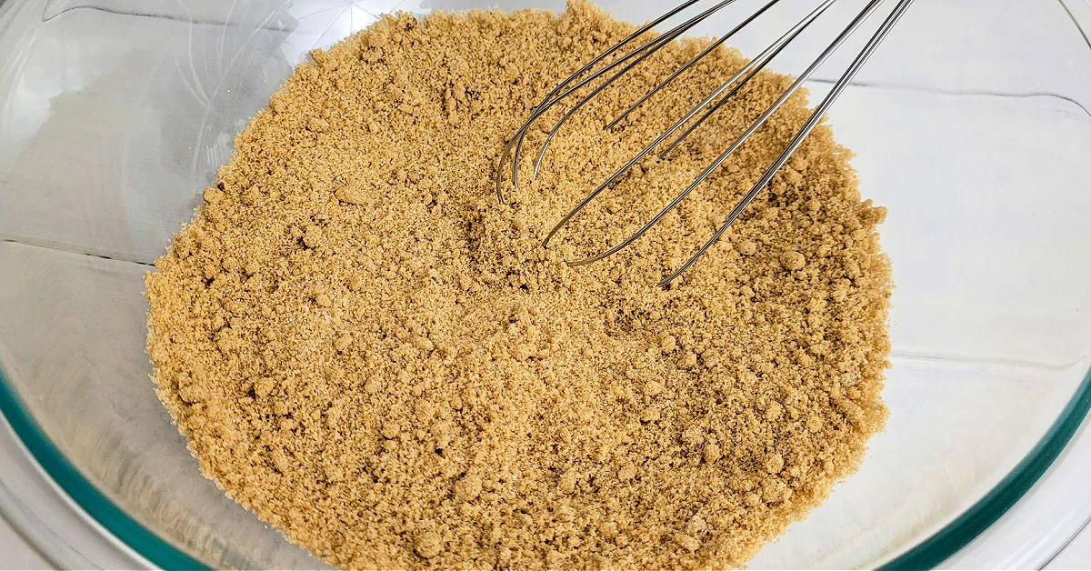 Brown and white sugars being whisked together in a large glass mixing bowl.