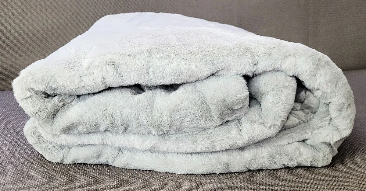Gravity faux rabbit fur weighted blanket folded up and set on the futon.