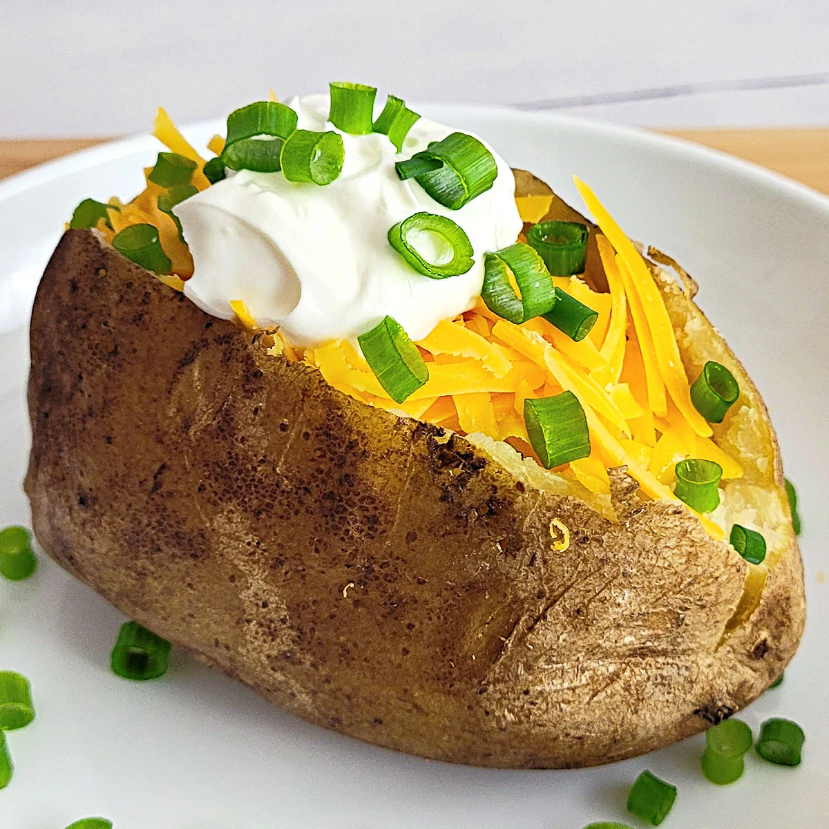 Baked potato topped with cheddar cheese, sour cream and sliced green onions.