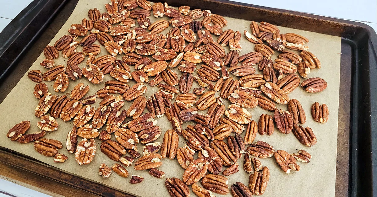 Toasted pecans on a parchment paper lined baking sheet.