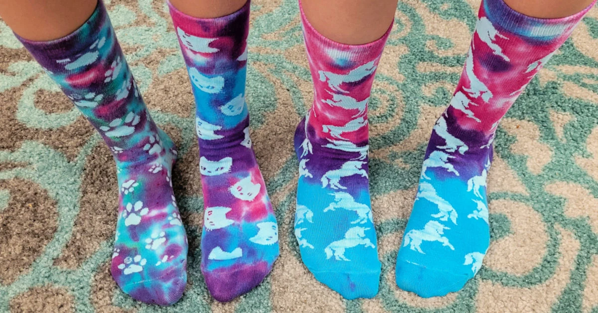 Tie dye socks on feet standing on a colorful rug.