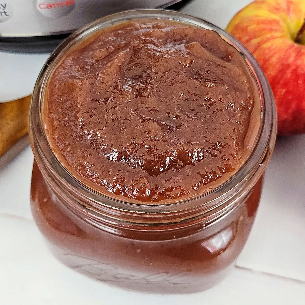 Apple butter in a pint jar next to an Instant Pot, apple and wood ladle.